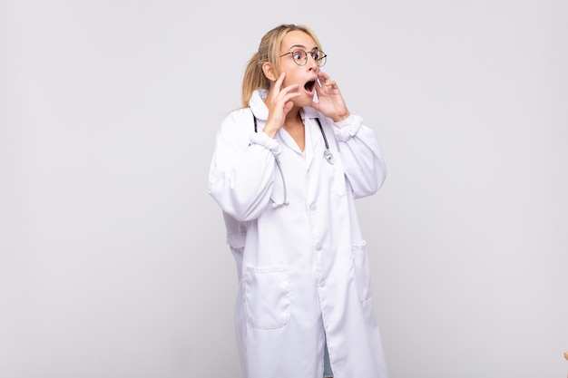 Young woman physician feeling happy, excited and surprised, looking to the side with both hands on face