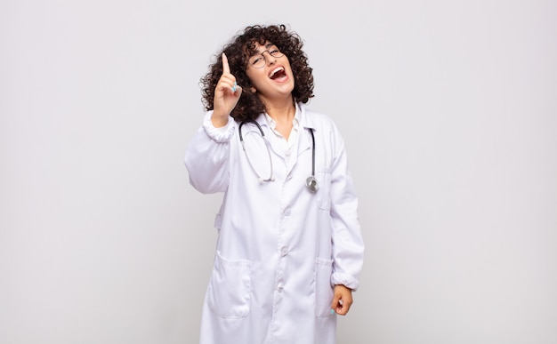 Young woman physician feeling like a happy and excited genius after realizing an idea, cheerfully raising finger, eureka!