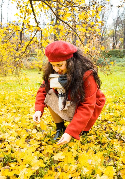 Foto giovane donna che raccoglie le foglie di autunno nel parco