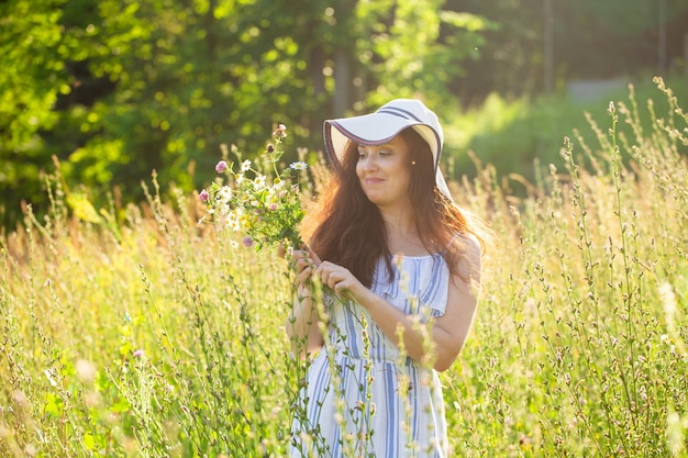 夏の夜に牧草地で花を摘む若い女性