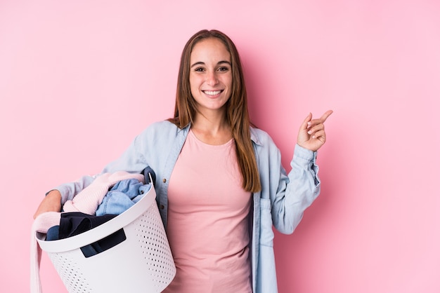 Young woman picking up dirty clothes smiling and pointing aside, showing something at blank space