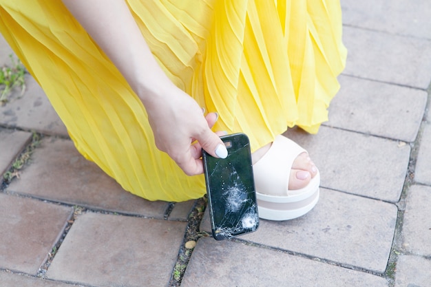 Young woman picks up a broken phone from the ground