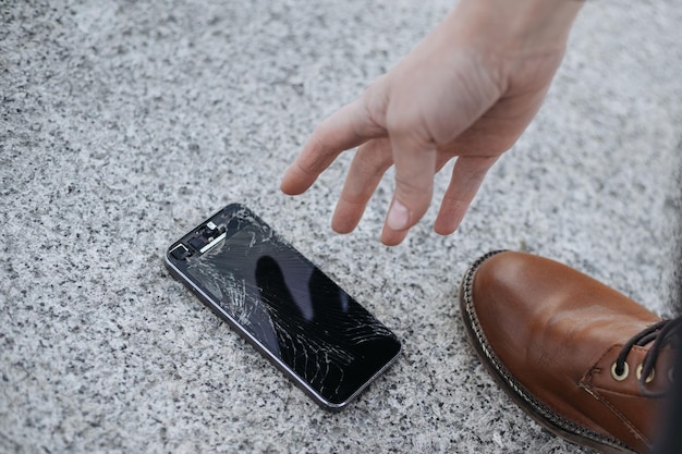 Young woman picks up her broken smartphone with cracked screen glass after huge falling