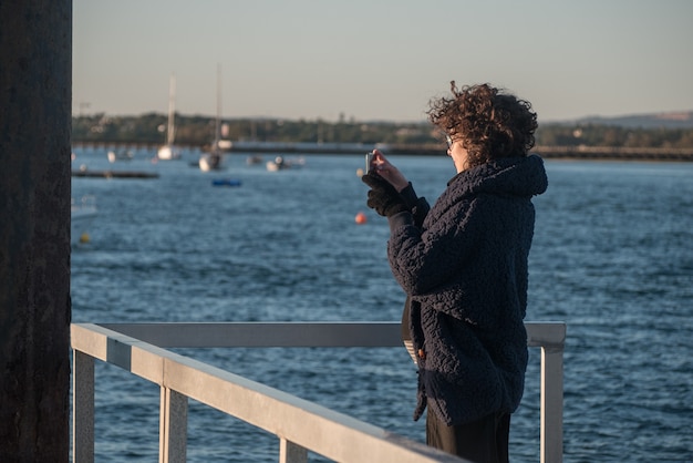 Giovane donna su un molo a scattare foto dal telefono cellulare.