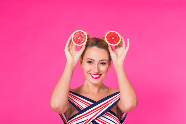 Young woman on a pink background holds a cut orange in her hands and laughs. Colour obsession concept.