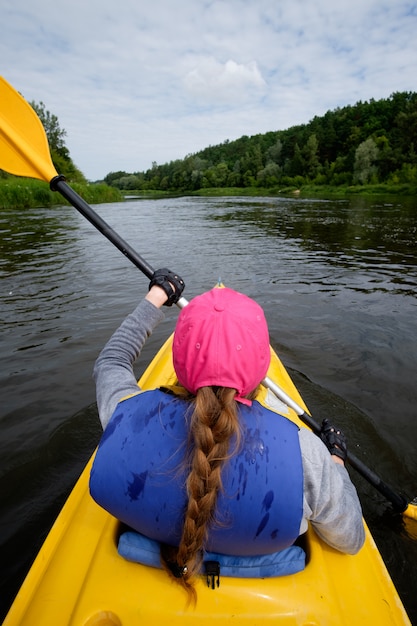 Young woman in pink cap rowing in kayak over the river