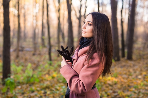秋の自然の上のピンクのコートを着た若い女性