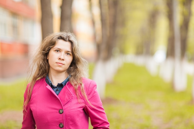 Young woman in pink coat standing in autumn park