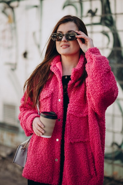 通りに立っているピンクのコートを着た若い女性