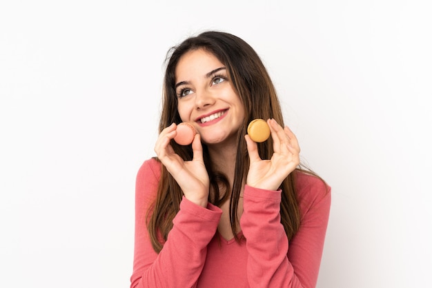 Young woman on pink holding colorful French macarons and looking up