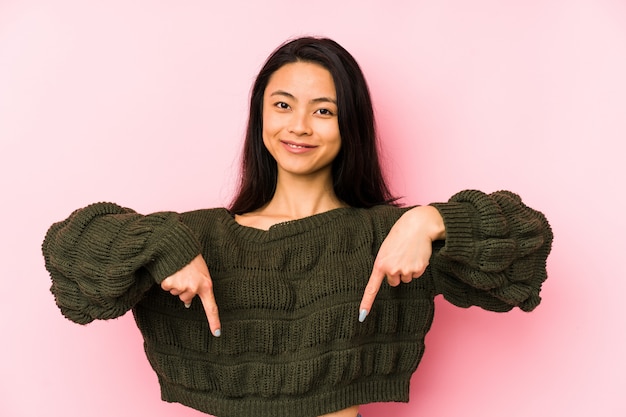 Young woman on a pink points down with fingers, positive feeling.