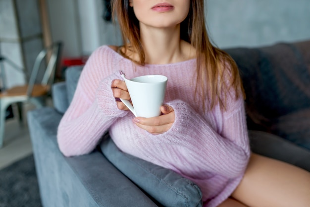 Una giovane donna in un maglione rosa tiene la tazza di caffè, primo piano