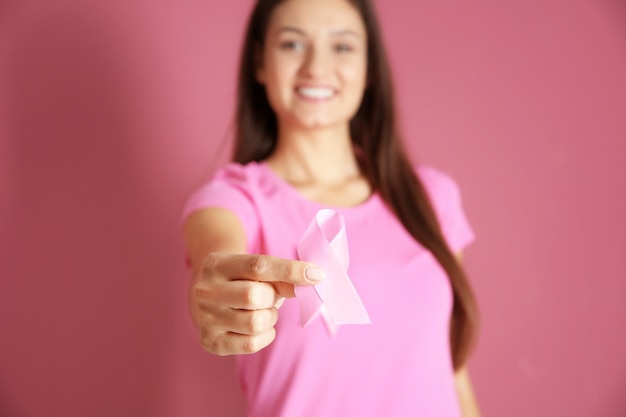 Foto giovane donna in maglietta rosa che tiene nastro su sfondo colorato concetto di consapevolezza del cancro al seno