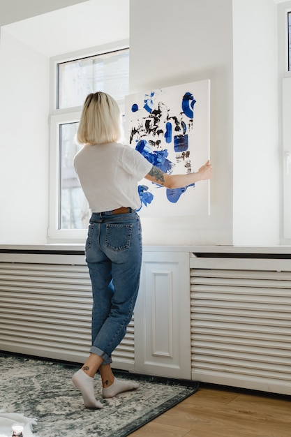 Photo young woman placing abstract paint on the wall