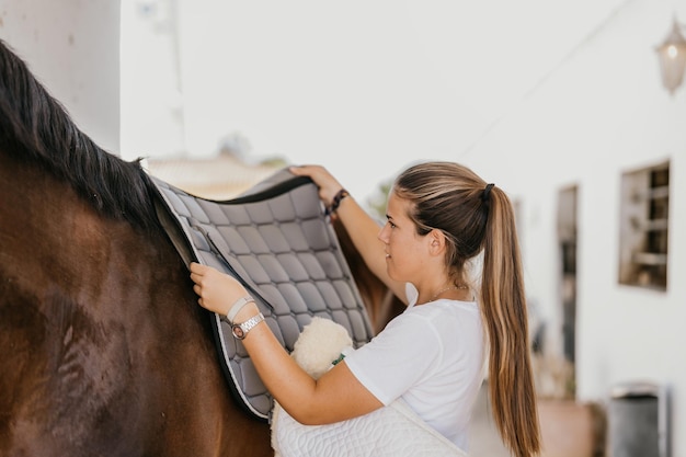 Young woman placing a blanket over the back of a horse to fit a saddle