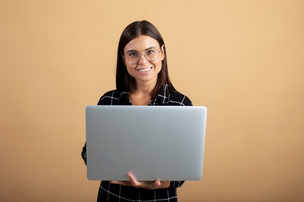 A young woman in a plaid dress stands on an orange  with a laptop