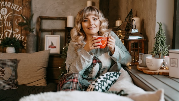 Young woman in plaid with cup of hot tea in a Christmas cozy interior The concept of preparation for the holidays Make a wish and dream