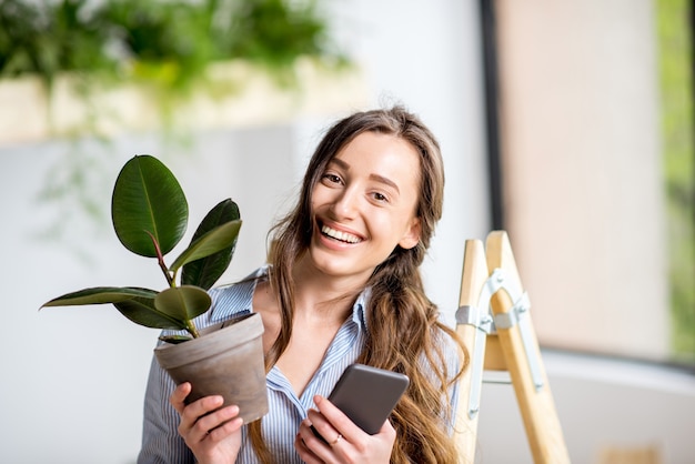 はしごに電話と植木鉢で立っている緑と家を植える若い女性