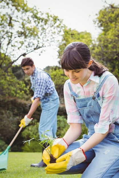 young woman planting a sapling in garden and man cleaning grass 