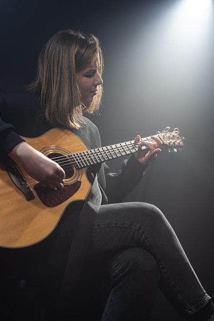 Giovane donna che suona la chitarra acustica in una stanza buia con foschia