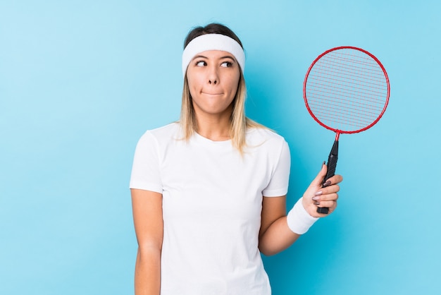 Young woman playing badminton confused, feels doubtful and unsure.