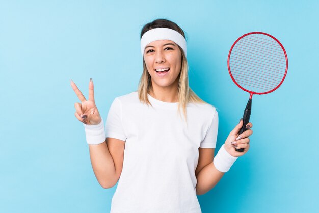 Young woman playing badminton isolated joyful and carefree showing a peace symbol with fingers