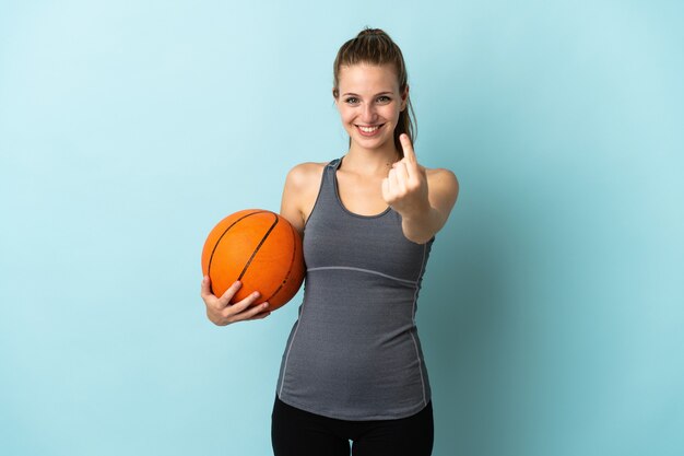 Young woman playing basketball isolated on blue background doing coming gesture