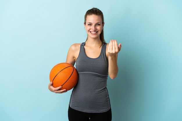 手で来るように誘う青い背景で隔離のバスケットボールをしている若い女性。あなたが来て幸せ
