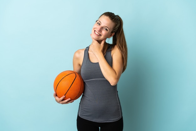 Молодая женщина играет в баскетбол, изолирована на синем, счастлива и улыбается