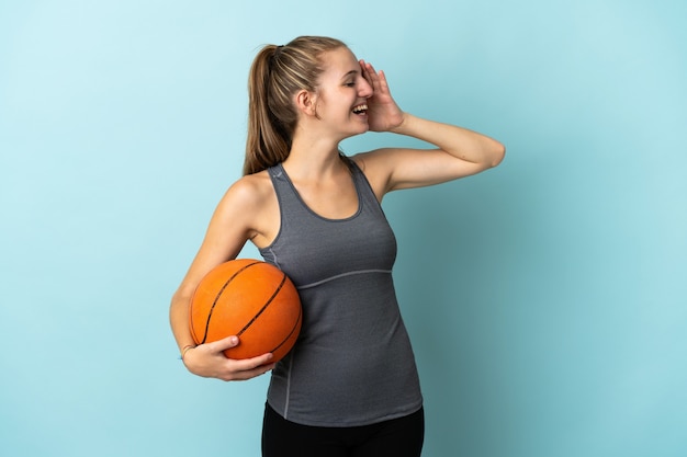 Young woman playing basketball isolated on blue wall smiling a lot