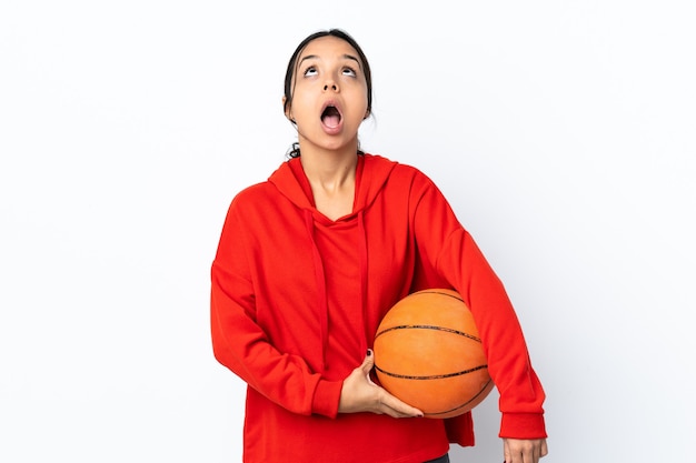 Young woman playing basketball isolated looking up and with surprised expression