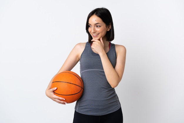 Young woman playing basketball isolated on white background looking to the side and smiling
