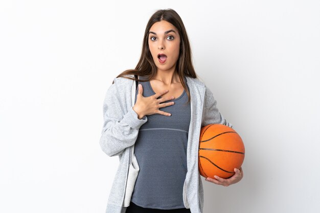 Giovane donna che gioca a basket isolato su sfondo bianco sorpreso e scioccato mentre guarda a destra