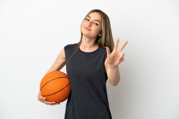 Giovane donna che gioca a basket su un muro bianco isolato felice e conta tre con le dita