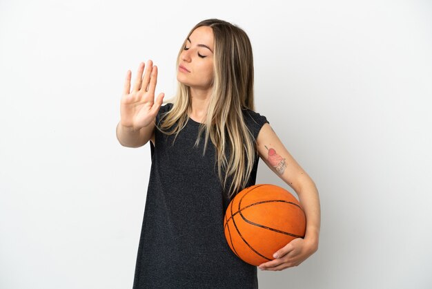 Молодая женщина играет в баскетбол над изолированной белой стеной, делая жест стоп и разочарованная