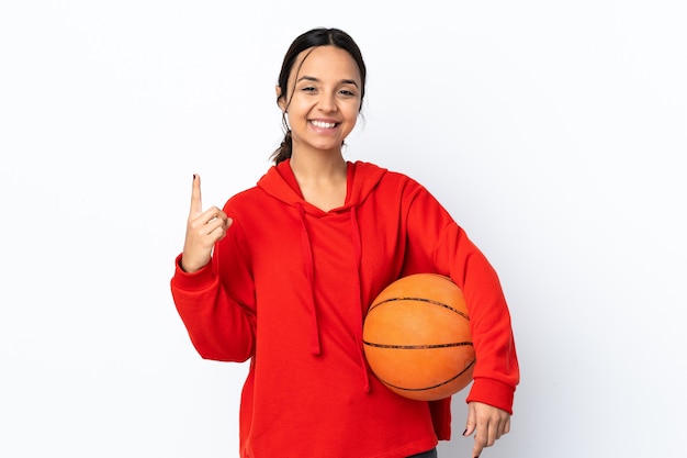 Young woman playing basketball over isolated white wall pointing up a great idea