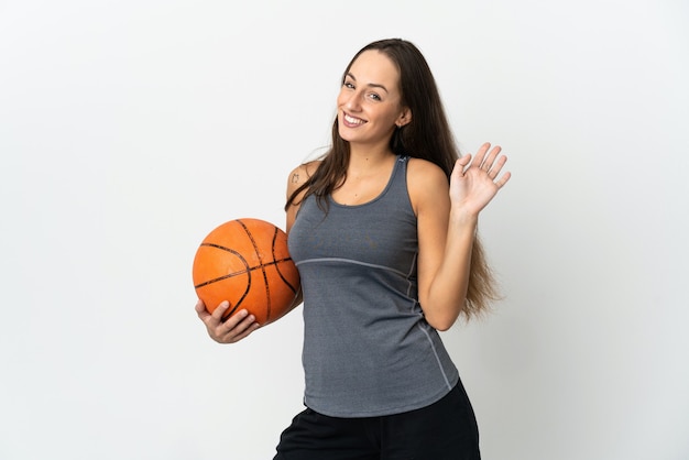 Young woman playing basketball over isolated white wall saluting with hand with happy expression