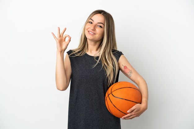 Young woman playing basketball over isolated white wall showing ok sign with fingers