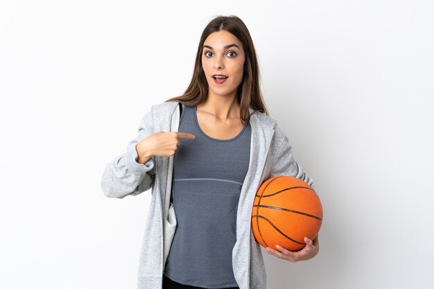 Young woman playing basketball isolated on white with surprise facial expression