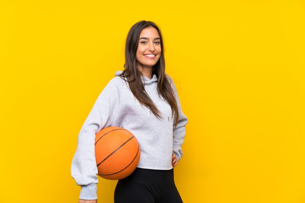 Young woman playing basketball over isolated yellow wall