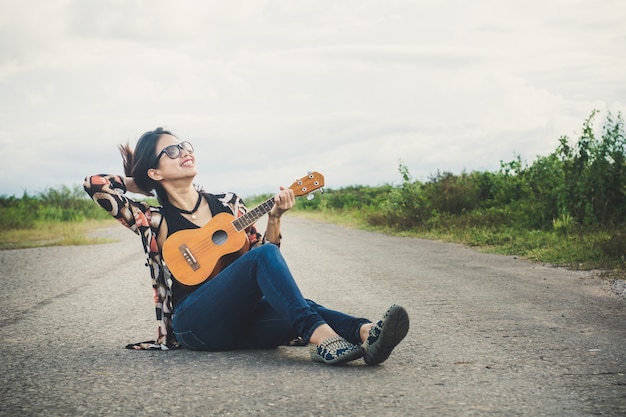 Young woman playing on brown Ukulele in the park.