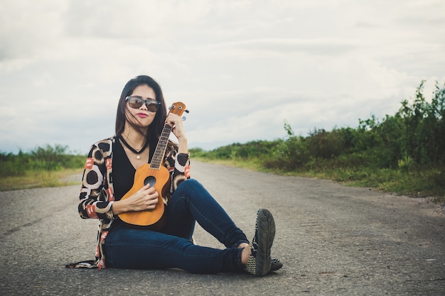 Photo young woman playing on brown ukulele in the park.