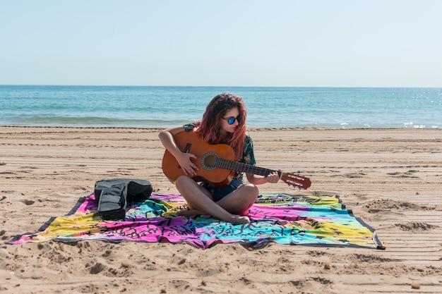 Giovane donna a suonare la chitarra sulla spiaggia