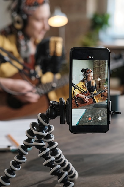 Young woman playing guitar during broadcasting on radio and recording content on mobile phone