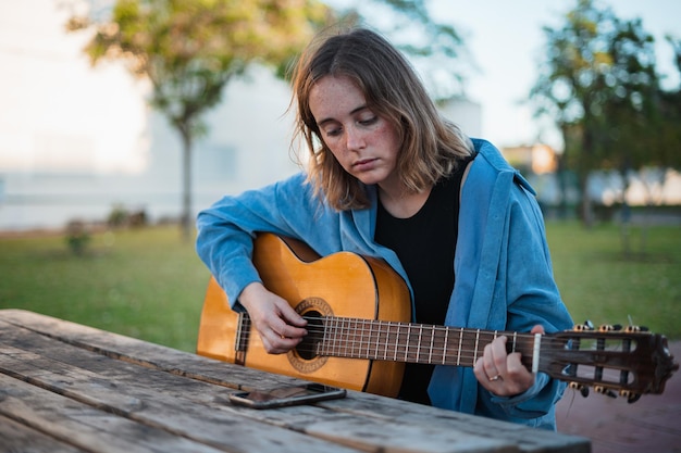 Young woman playing guitar at picnic table