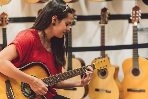 Young woman playing a guitar in a shop surrounded by spanish\
guitars