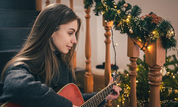 A young woman playing guitar sitting on the steps at home