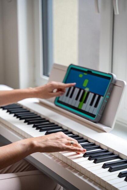 Young woman playing a keyboard while pointing at a learning app on a tablet technology enhances