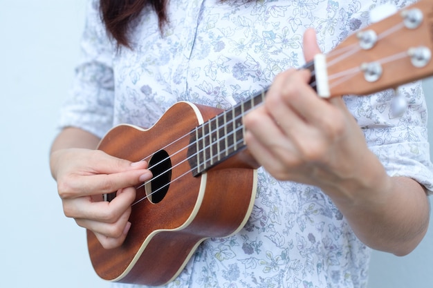 Фото Молодая женщина, играя на коричневом ukulele в белом или сером фоне.