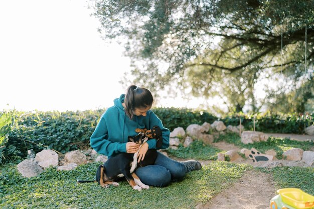 Foto giovane donna che gioca con grandi cuccioli in grembo mentre è seduta sull'erba verde